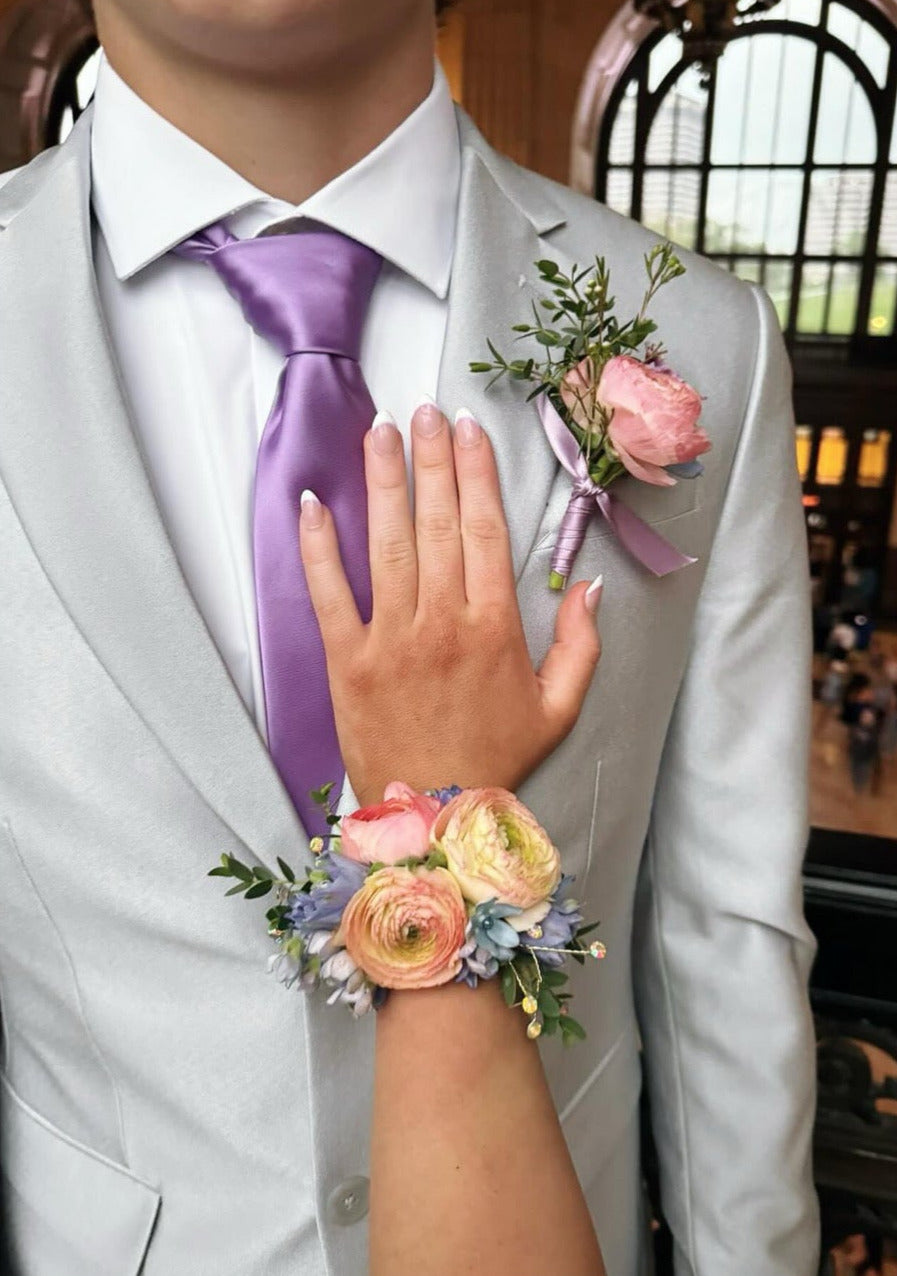 Person in formal attire with a purple tie and floral wrist corsage, standing in a decorated indoor setting.