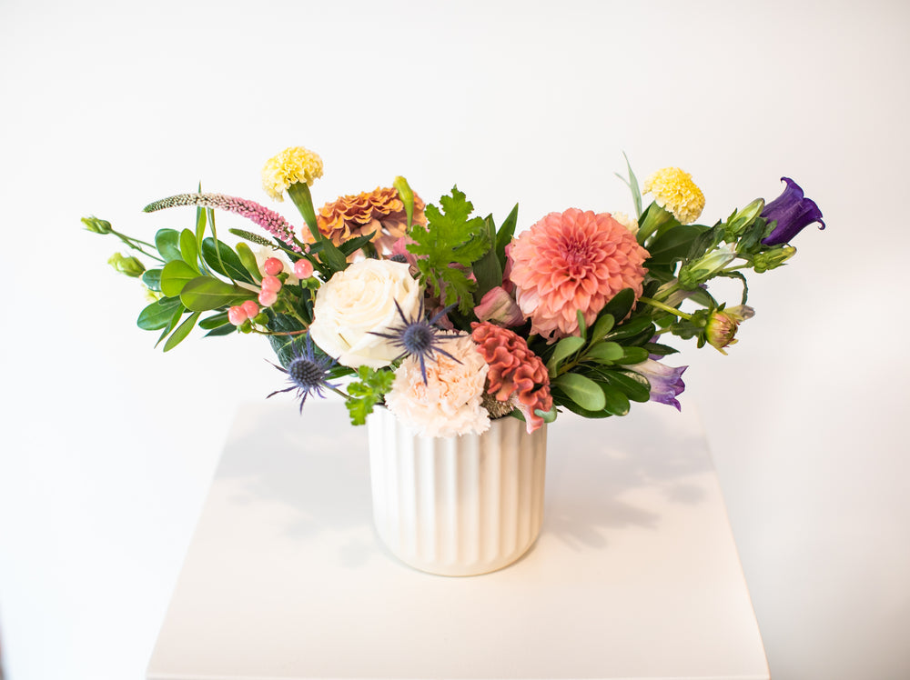 Colorful flower arrangement in a white vase on a light surface with a white background