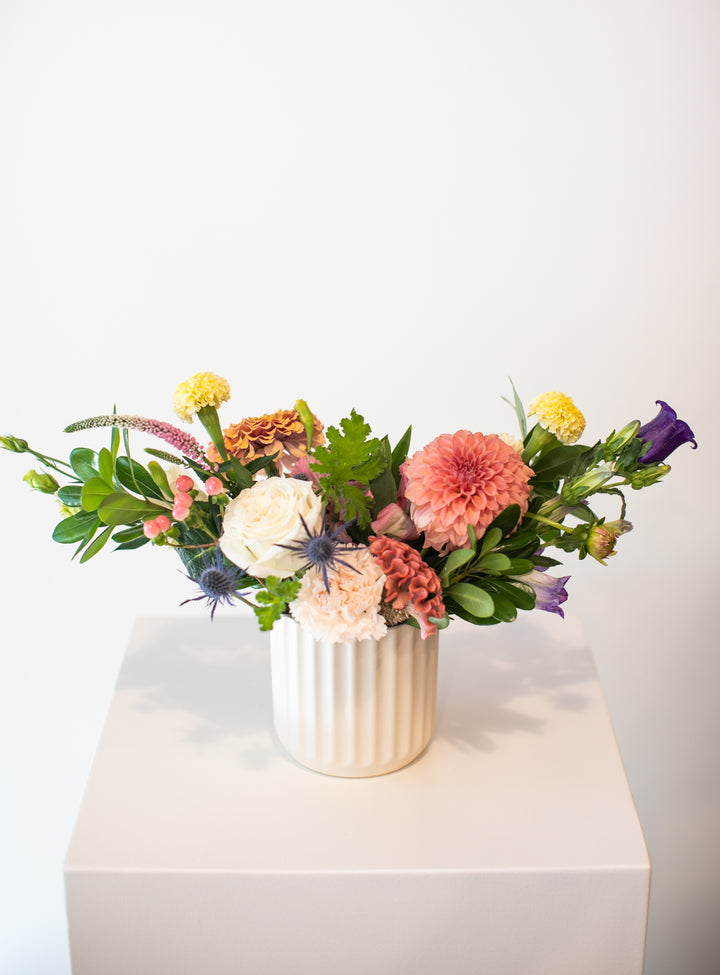 Colorful flower arrangement in a white vase on a white surface with a white background