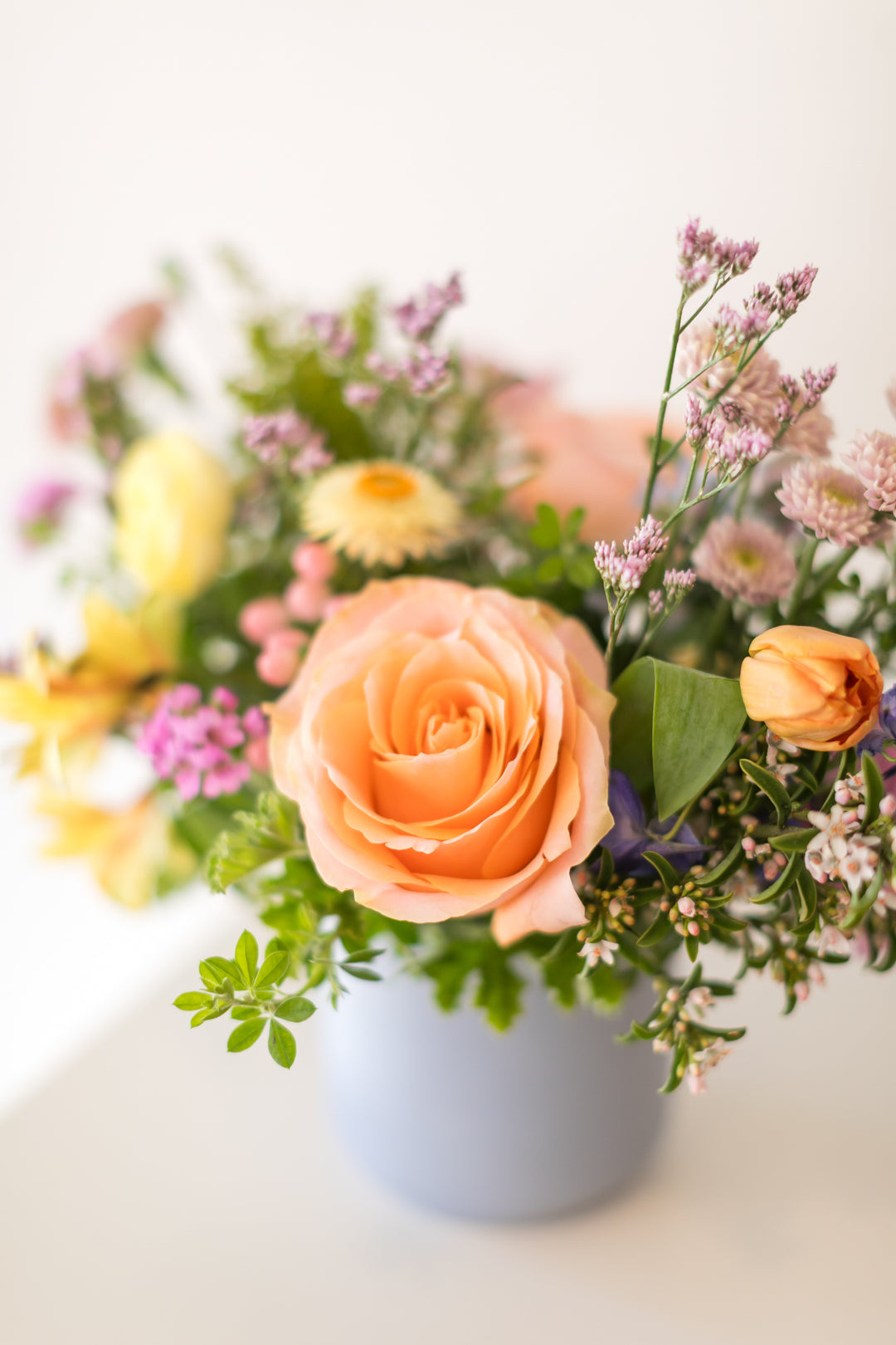 Floral arrangement with orange roses and greenery in a light blue vase Kansas City Florist